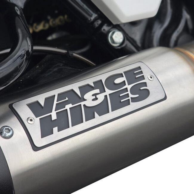Close-up of a motorcycle exhaust can with a Vance & Hines logo plate on it, chrome finish visible.