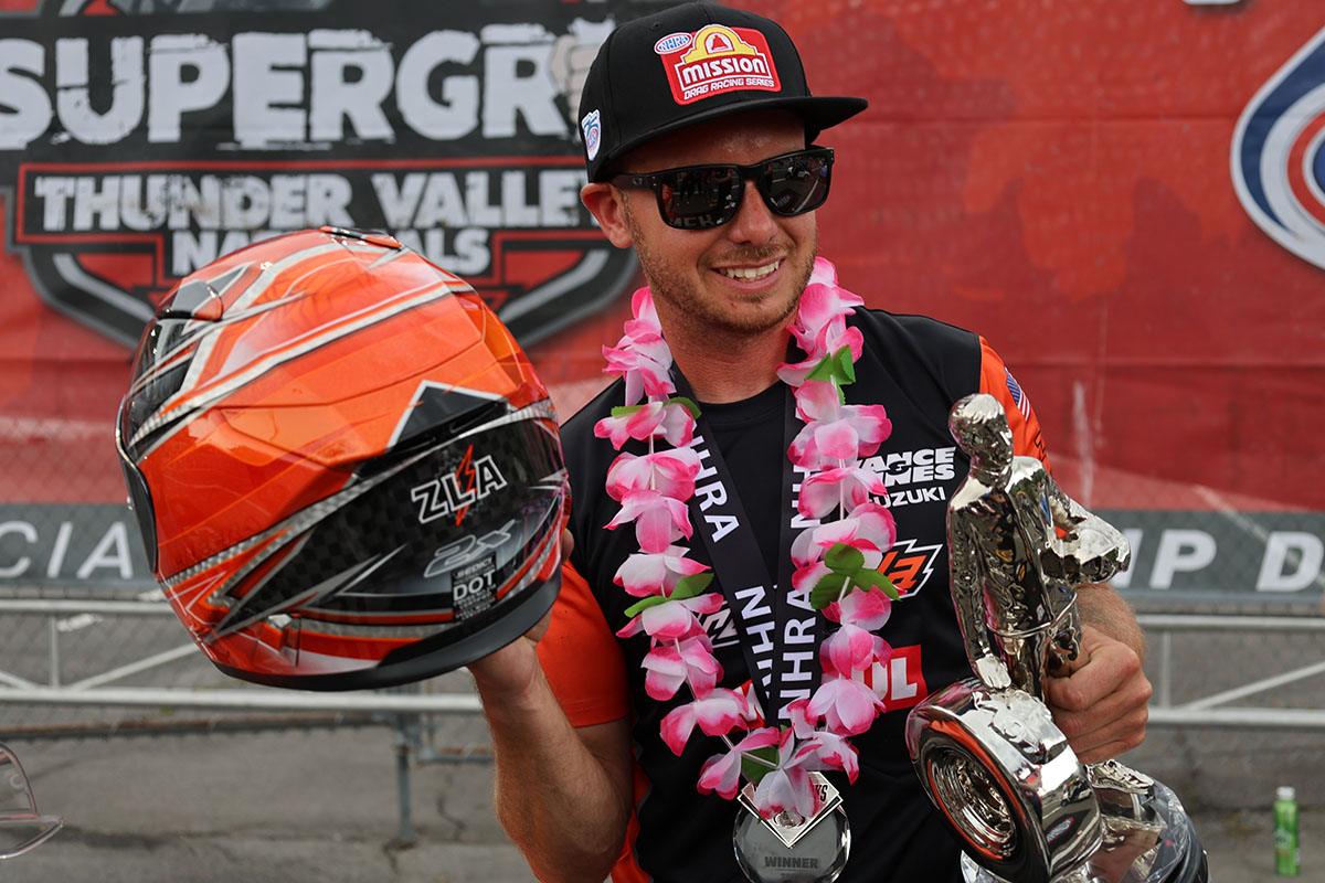IMG_7159-sm | Vance & Hines Motorsports Motorsport winner wearing sunglasses and a cap, holding a metallic trophy and an orange helmet with a pink leis around his neck.